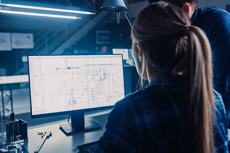 Engineer Working on Desktop Computer, Screen Showing CAD Software with Technical Blueprints, Her Male Project Manager Explains Job Specifics. Industrial Design Engineering Facility Office